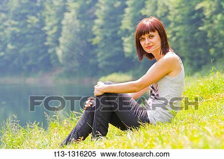 Young woman is resting on the grass next to a river View Large Photo Image Stock Photography - Young woman is resting on the grass next to a river. Fotosearch