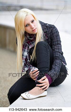 Stock Image - Young woman is sitting and holding leg. Fotosearch