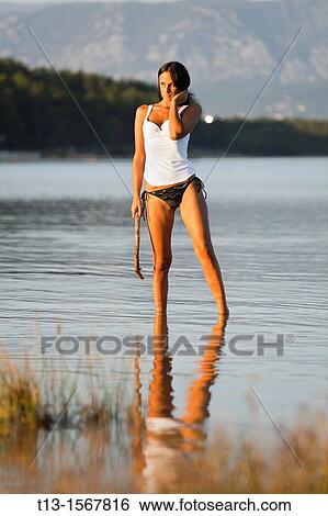 Young woman is standing in a shallow water with a tree branch in hand View Large Photo Image Stock Photograph - Young woman is standing in a shallow water with a tree branch in hand. Fotosearch