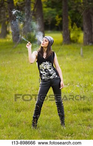 Stock Photograph - Young woman is standing in forest meadow and smoking a cigarette with smoke clearly shown. Fotosearch