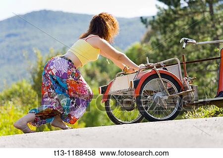Young woman is trying hard to push a three-wheeler away from a road View Large Photo Image Stock Photo - Young woman is trying hard to push a three-wheeler away from a road. Fotosearch