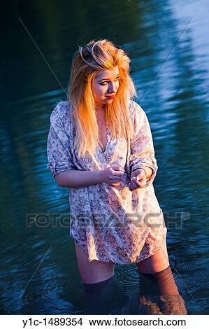 Picture - Young woman is watching sunset while standing in the water. Fotosearch