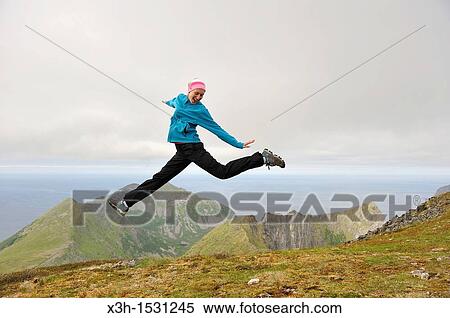Stock Photography - young woman jumping at the top of the Husfjellet mountain, Senja island County of Troms, Norway, Northern Europe. Fotosearch