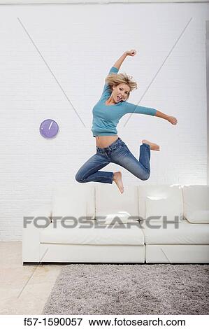Stock Photo - Young woman jumping for joy off her sofa. Fotosearch