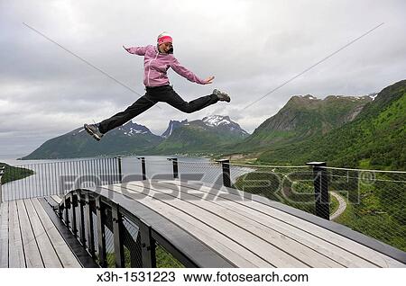 young woman jumping over the fjord Bergsfjorden Landscaping of the National Tourist Route The west coast of the island Senja has been selected as one of the most spectacular landscapes in Norway Senja island County of Troms, Norway, Northern Europe View Large Photo Image Stock Image - young woman jumping over the fjord Bergsfjorden Landscaping of the National Tourist Route The west coast of the island Senja has been selected as one of the most spectacular landscapes in Norway Senja island County of Troms, Norway, Northern Europe. Fotosearch