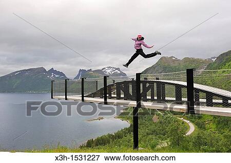 Stock Photo - young woman jumping over the fjord Bergsfjorden Landscaping of the National Tourist Route The west coast of the island Senja has been selected as one of the most spectacular landscapes in Norway Senja island County of Troms, Norway, Northern Europe. Fotosearch