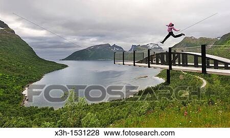 young woman jumping over the fjord Bergsfjorden Landscaping of the National Tourist Route The west coast of the island Senja has been selected as one of the most spectacular landscapes in Norway Senja island County of Troms, Norway, Northern Europe View Large Photo Image Stock Photo - young woman jumping over the fjord Bergsfjorden Landscaping of the National Tourist Route The west coast of the island Senja has been selected as one of the most spectacular landscapes in Norway Senja island County of Troms, Norway, Northern Europe. Fotosearch