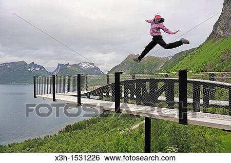 young woman jumping over the fjord Bergsfjorden Landscaping of the National Tourist Route The west coast of the island Senja has been selected as one of the most spectacular landscapes in Norway Senja island County of Troms, Norway, Northern Europe View Large Photo Image Stock Photograph - young woman jumping over the fjord Bergsfjorden Landscaping of the National Tourist Route The west coast of the island Senja has been selected as one of the most spectacular landscapes in Norway Senja island County of Troms, Norway, Northern Europe. Fotosearch