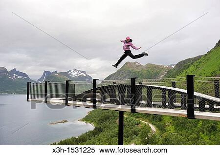 young woman jumping over the fjord Bergsfjorden Landscaping of the National Tourist Route The west coast of the island Senja has been selected as one of the most spectacular landscapes in Norway Senja island County of Troms, Norway, Northern Europe View Large Photo Image Stock Photography - young woman jumping over the fjord Bergsfjorden Landscaping of the National Tourist Route The west coast of the island Senja has been selected as one of the most spectacular landscapes in Norway Senja island County of Troms, Norway, Northern Europe. Fotosearch