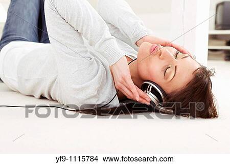 Picture - Young woman listening music lying on floor.. Fotosearch
