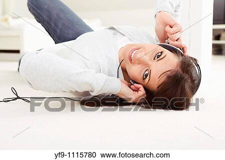 Stock Image - Young woman listening music lying on floor.. Fotosearch