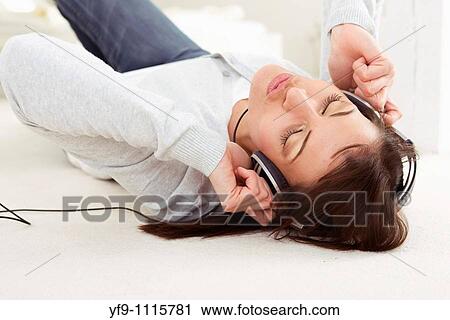 Stock Image - Young woman listening music lying on floor.. Fotosearch