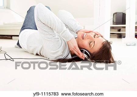 Stock Image - Young woman listening music lying on floor.. Fotosearch