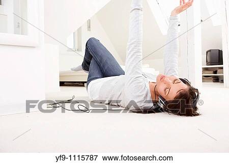 Stock Photo - Young woman listening music lying on floor.. Fotosearch