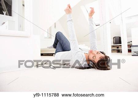 Stock Photo - Young woman listening music lying on floor.. Fotosearch