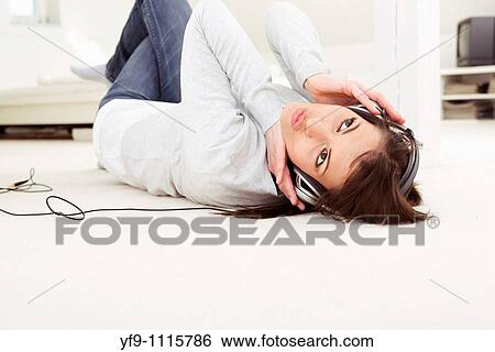 Stock Photograph - Young woman listening music lying on floor.. Fotosearch