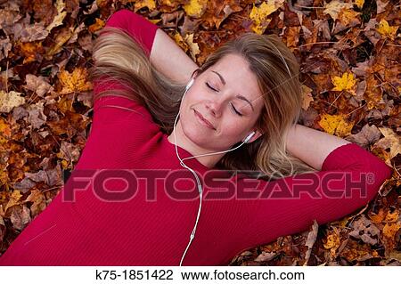 Young woman listening to music lying on a lawn of leaves View Large Photo Image Stock Image - Young woman listening to music lying on a lawn of leaves. Fotosearch