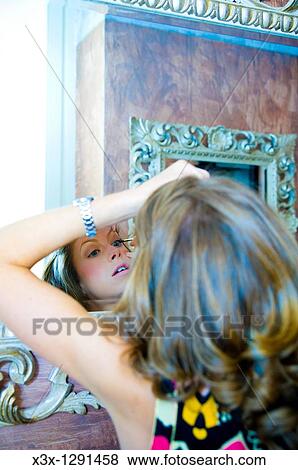 Stock Photo - young woman looking in mirror applying mascara. Fotosearch