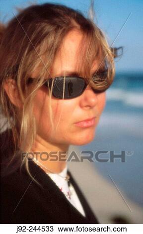 Stock Image - Young woman looking into the distance. Sunglasses reflect departing man.. Fotosearch