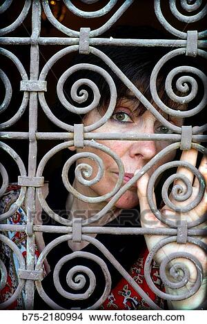 Picture - Young woman looking through a fence of a window in the Medina of Fez, Morocco, Africa.. Fotosearch