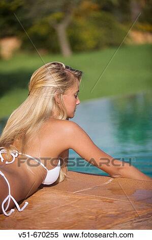 Young woman lying down on the deck of a pool touching surface of water View Large Photo Image Stock Photography - Young woman lying down on the deck of a pool touching surface of water. Fotosearch