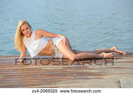 Stock Photography - Young woman lying on a jetty at a lake in Austria.. Fotosearch