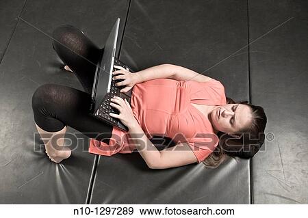 Young woman lying on a mat, working on her laptop computer View Large Photo Image Stock Photo - Young woman lying on a mat, working on her laptop computer. Fotosearch