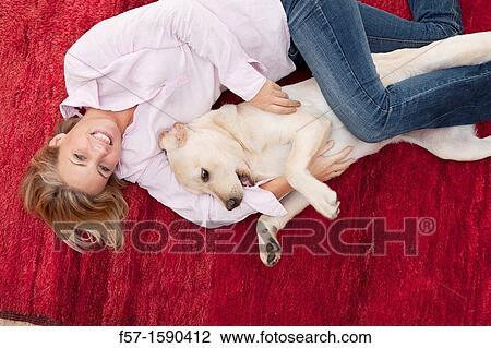 Stock Image - Young woman lying on a red carpet with her dog. Fotosearch