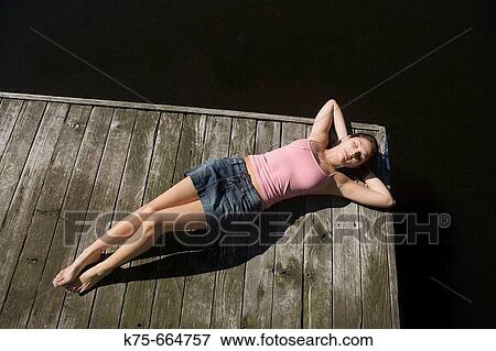 Young woman lying on dock, listening to music View Large Photo Image Stock Photo - Young woman lying on dock, listening to music. Fotosearch