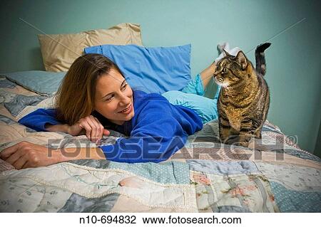 Young woman lying on her bed next to her pet cat View Large Photo Image Stock Image - Young woman lying on her bed next to her pet cat. Fotosearch