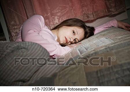 Young woman lying on her bed. View Large Photo Image Picture - Young woman lying on her bed.. Fotosearch