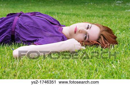 Stock Image - Young woman lying on the grass in a park. Fotosearch