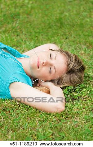 Stock Image - Young woman lying on the park listening to mp3 player. Fotosearch