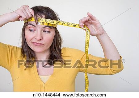Young woman measuring the size of her head with a tape measure View Large Photo Image Picture - Young woman measuring the size of her head with a tape measure. Fotosearch