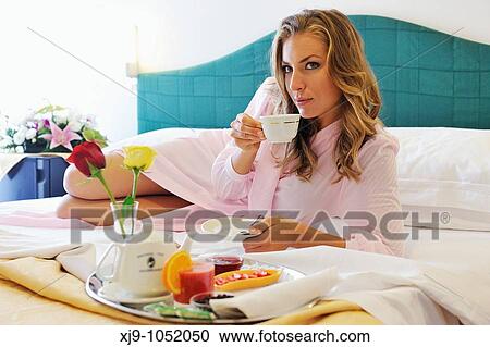 Stock Image - Young woman on bed in hotel room. Fotosearch