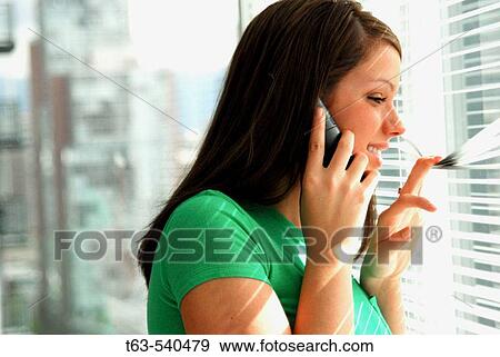 young woman on cell phone peeking through blinds View Large Photo Image Stock Photo - young woman on cell phone peeking through blinds. Fotosearch
