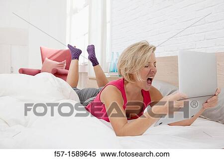 Young woman on her bed exasperated with her laptop View Large Photo Image Stock Photography - Young woman on her bed exasperated with her laptop. Fotosearch