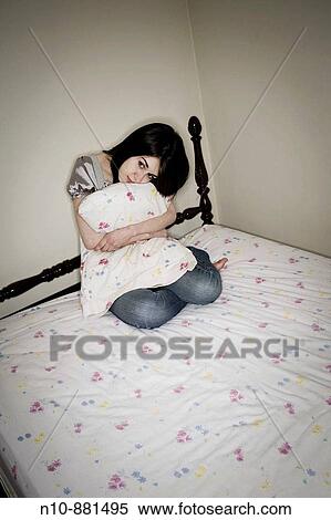 Stock Photography - Young woman on her bed, holding a pillow. Model and Property Released.. Fotosearch
