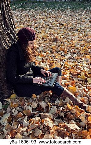 Young woman outdoors sitting on autumn leaves using laptop View Large Photo Image Stock Image - Young woman outdoors sitting on autumn leaves using laptop. Fotosearch
