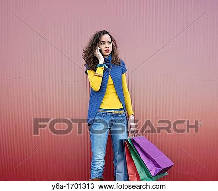 Stock Image - Young woman outdoors with shopping bags talking on mobile phone. Fotosearch
