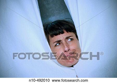 Stock Image - Young woman peeking out from behind a pair of curtains. Fotosearch