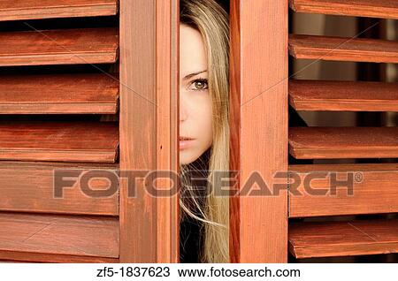 Stock Image - Young woman peeking through the window. Fotosearch