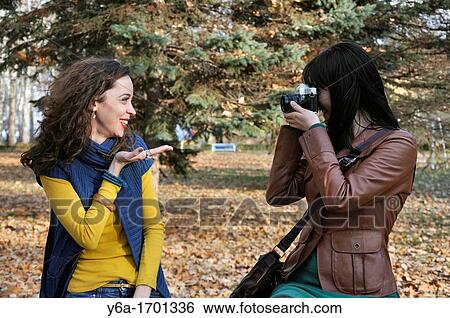 Stock Photograph - Young woman photographing her friend in park. Fotosearch