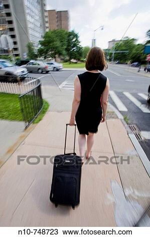 Stock Image - Young woman pulling a rolling suitcase.. Fotosearch