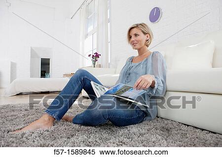 Stock Photography - Young woman reading in her living room. Fotosearch