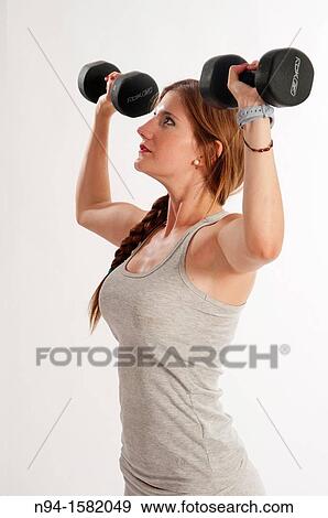Stock Photo - Young woman, redhead, exercising with weights in the gym to get fit. Fotosearch