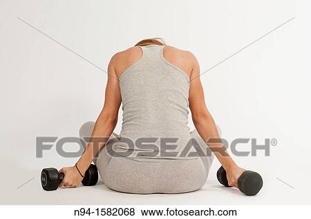 Stock Photo - Young woman, redhead, sitting, exercising with weights at the gym. Fotosearch