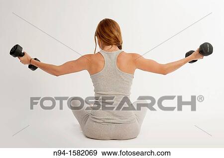 Stock Photo - Young woman, redhead, sitting, exercising with weights at the gym. Fotosearch