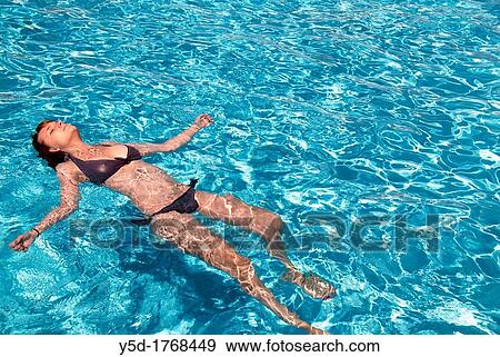 Stock Photo - young woman relaxed laying in the water in swimming pool. Fotosearch