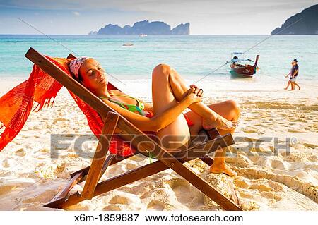 Stock Photo - Young woman relaxing on a deckchair Long beach Phi Phi Don island Krabi province, Andaman Sea, Thailand. Fotosearch